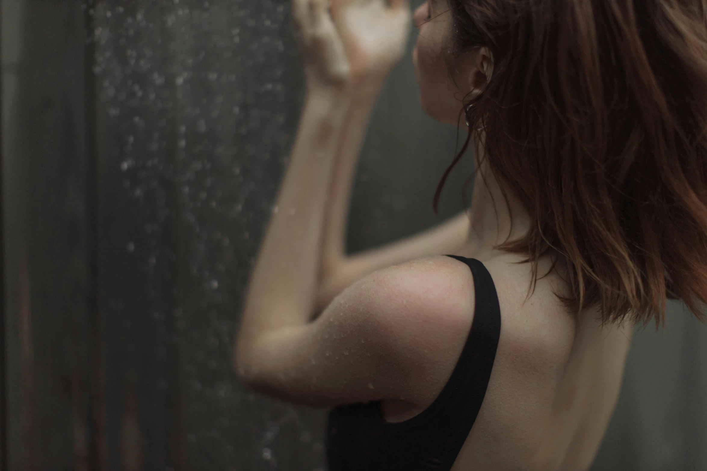 a woman in a black dress standing in front of a shower, inspired by Elsa Bleda, pexels contest winner, renaissance, swollen muscles, a redheaded young woman, rainy afternoon, showing her shoulder from back