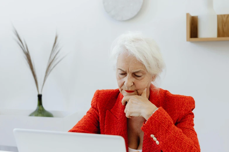 a woman sitting in front of a laptop computer, a photo, trending on pexels, an old lady with red skin, royal commission, red and white neon, on a white table