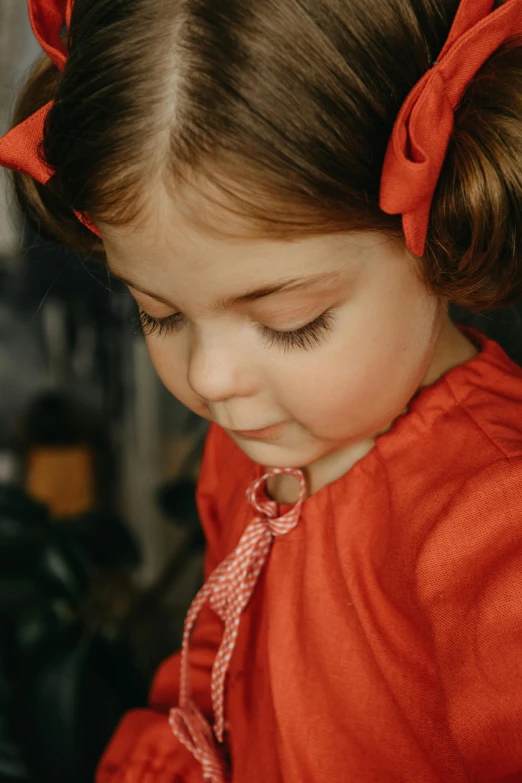 a little girl with a red bow on her head, inspired by Kate Greenaway, pexels contest winner, close up shot from the side, wearing red clothes, shy looking down, wearing collar