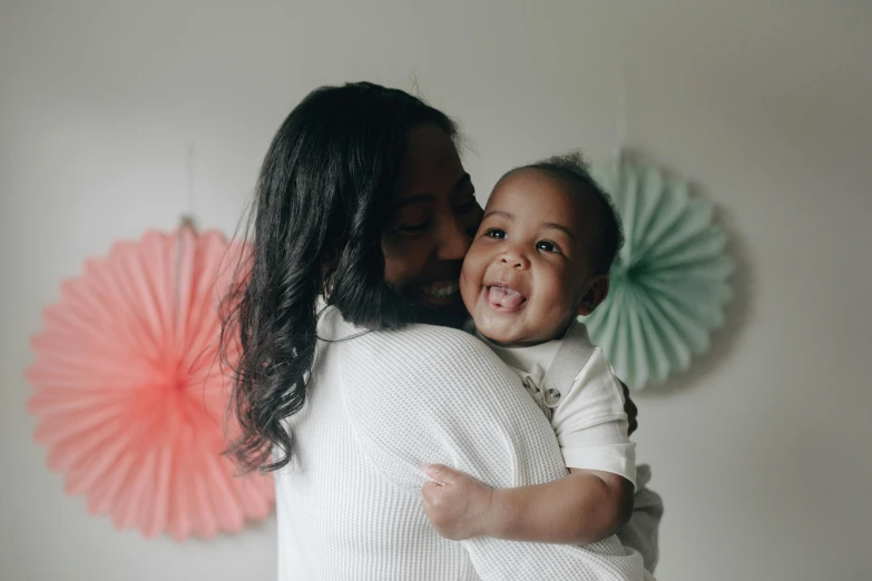 a woman holding a baby in her arms, by Arabella Rankin, pexels contest winner, happening, black, a still of a happy, rosey cheeks, coloured