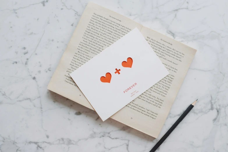 a couple of cards sitting on top of an open book, by Julia Pishtar, private press, rose gold heart, orange and white, library of forever, simple design