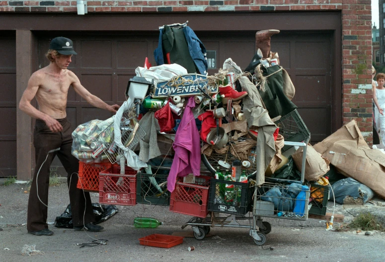 a man standing next to a pile of garbage, a photo, by Jonathan Solter, maximalism, cart, donald trump as a homeless man, photography of bill brauer, 2010s
