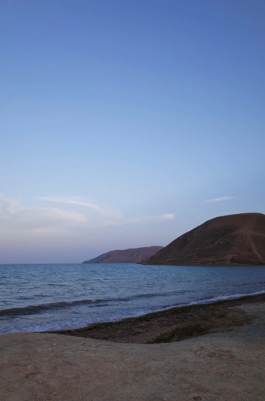 a large body of water sitting on top of a sandy beach, by Daren Bader, les nabis, the dead sea, dusk, light blue water, hills