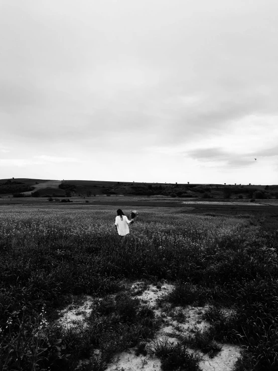 a person standing in a field flying a kite, a black and white photo, by Lucia Peka, unsplash, panoramic view of girl, shot with iphone 1 0, medium format. soft light, jovana rikalo