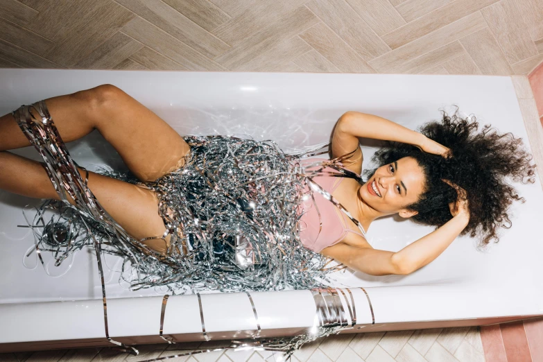 a woman laying in a bathtub covered in tinsel, trending on pexels, chrome outfit, nathalie emmanuel, annoying sister vibes, full body image