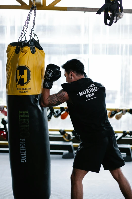 a man hitting a punching bag in a gym, by Robbie Trevino, black and yellow, manuka, bags, full colour