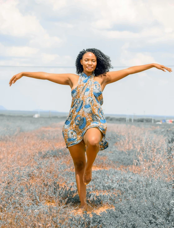 a woman standing in a field with her arms outstretched, pexels contest winner, happening, wearing an african dress, tan skin a tee shirt and shorts, posing for a picture, at full stride