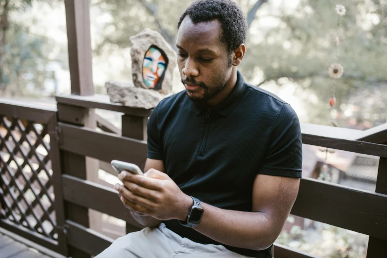 a man sitting on a bench looking at his cell phone, man is with black skin, uploaded, avatar image, portrait featured on unsplash