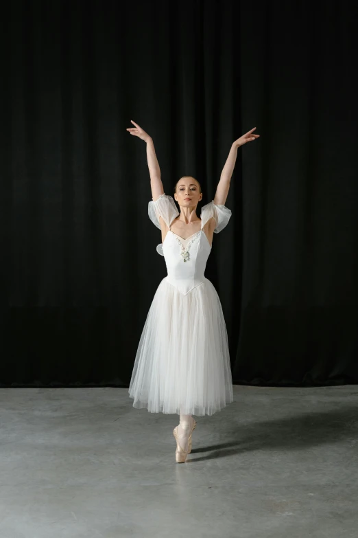 a woman in a white dress standing in front of a black curtain, a portrait, by Elizabeth Polunin, unsplash, arabesque, wearing a tutu, with arms up, portrait n - 9, slide show