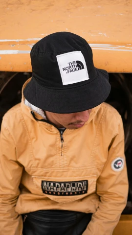 a man in a yellow jacket and a black hat, unsplash, bucket hat, square sticker, main colour - black, nepal