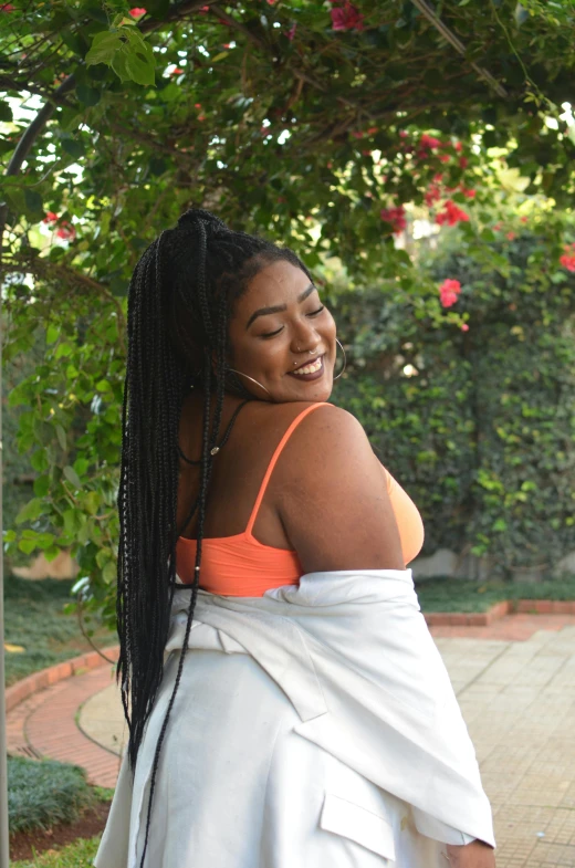 a woman in an orange top and white skirt, an album cover, inspired by Esaias Boursse, unsplash, alluring plus sized model, wearing a towel, long black braids, relaxing and smiling at camera