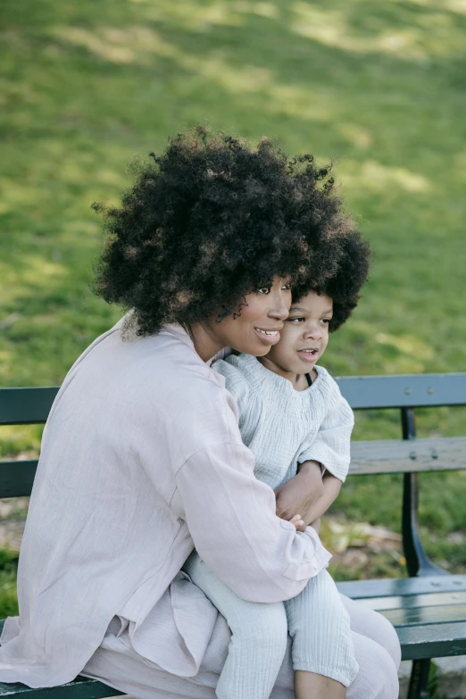 a woman and child sitting on a bench in a park, by Lily Delissa Joseph, pexels contest winner, natural hair, curls on top of his head, slightly minimal, soft details