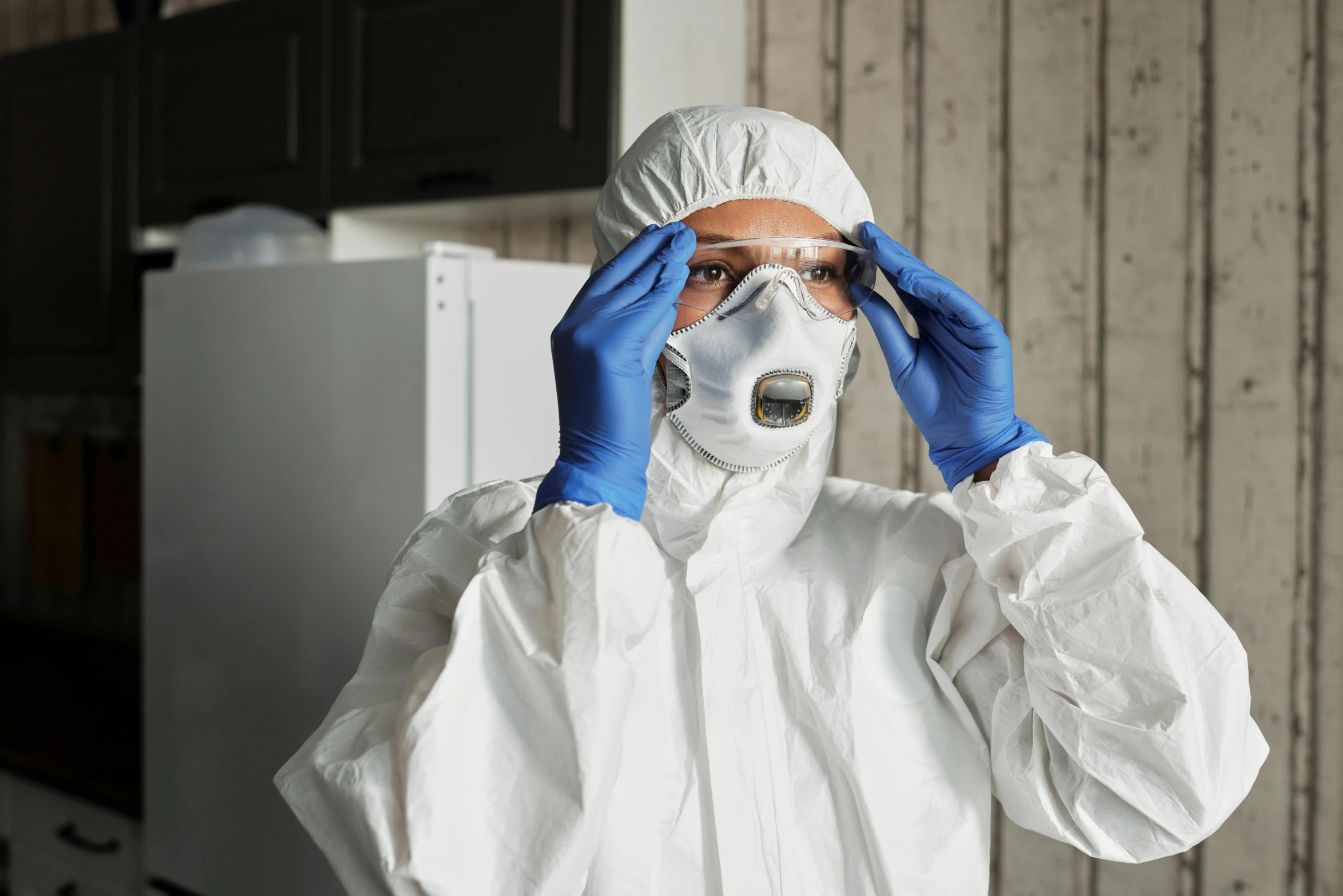 a person wearing a white suit and blue gloves, plasticien, concerned, respirator, at home, lab coat