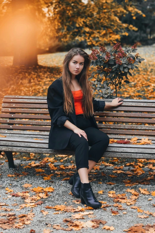 a woman sitting on top of a wooden bench, by Julia Pishtar, pexels contest winner, black and orange coat, attractive young woman, 15081959 21121991 01012000 4k, autum garden