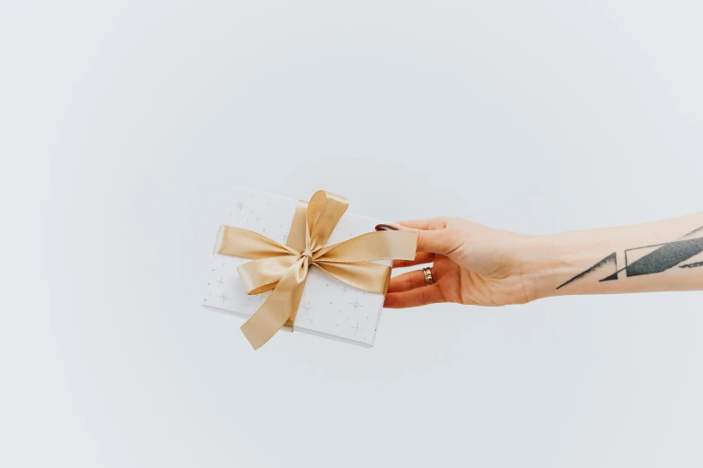 a woman's hand holding a gift wrapped in brown ribbon, by Emma Andijewska, pexels contest winner, minimalism, white with gold accents, gif, rectangle, small