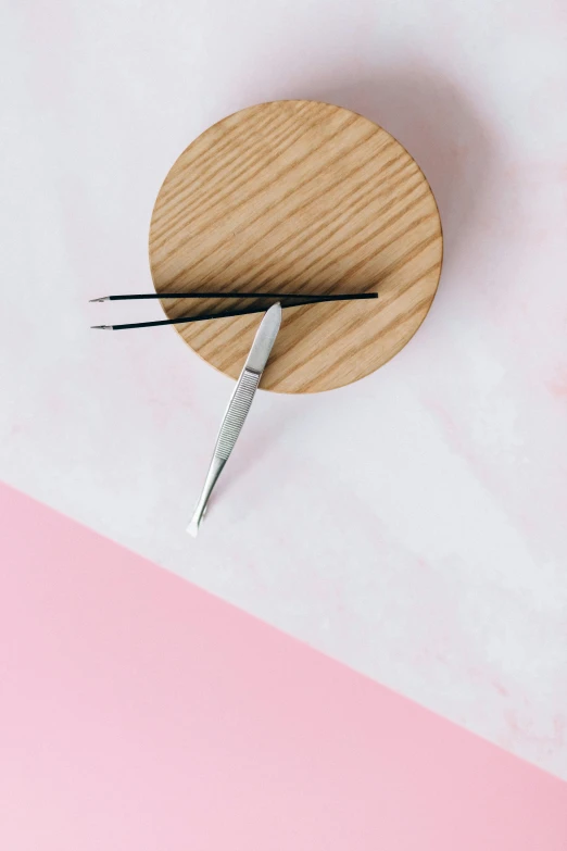 a wooden clock sitting on top of a pink and white surface, by Paul Bird, trending on pexels, new objectivity, surgical implements, made of brushed steel, small quills along it's back, close-up product photo