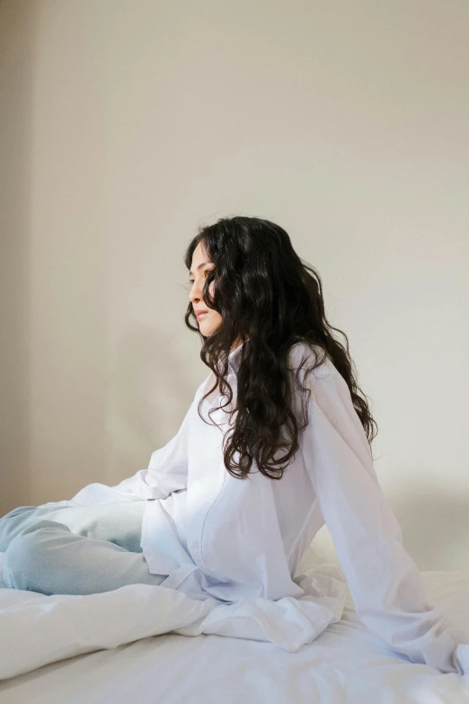 a woman sitting on top of a bed next to a window, by Kim Tschang Yeul, trending on unsplash, happening, long curly black hair, wearing white pajamas, profile pic, plain background