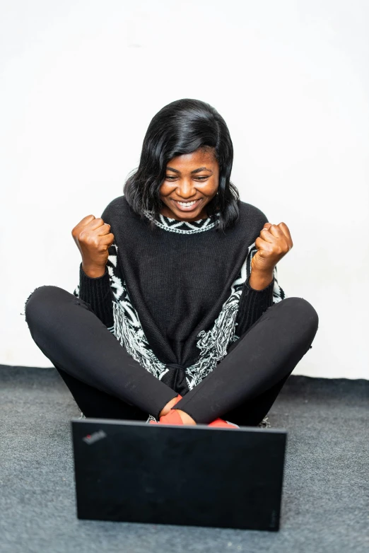 a woman sitting on the floor with her laptop, inspired by Chinwe Chukwuogo-Roy, pexels contest winner, happening, cheering, wearing a black sweater, programming, sitting on bent knees