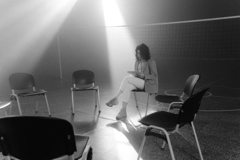 a black and white photo of a woman sitting in a chair, by Maurycy Gottlieb, pexels, in the high school gym, a seance, multiple lights, 7 0 s photo