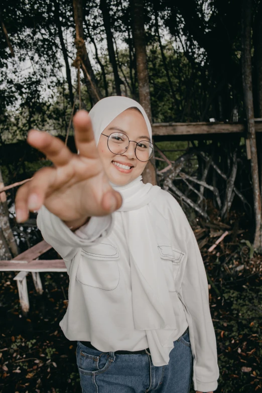 a woman standing in front of a wooden fence, a picture, unsplash, hurufiyya, wave a hand at the camera, malaysian, wearing square glasses, ((portrait))