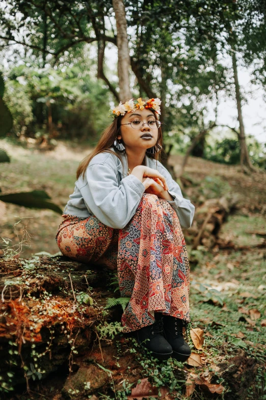 a woman sitting on top of a tree stump, an album cover, inspired by Ruth Jên, sumatraism, wearing a floral crown, thoughtful pose, patterned clothing, profile image