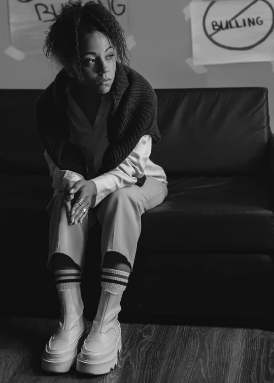 a black and white photo of a woman sitting on a couch, ashteroth, with depressive feeling, wearing adidas clothing, trending photo