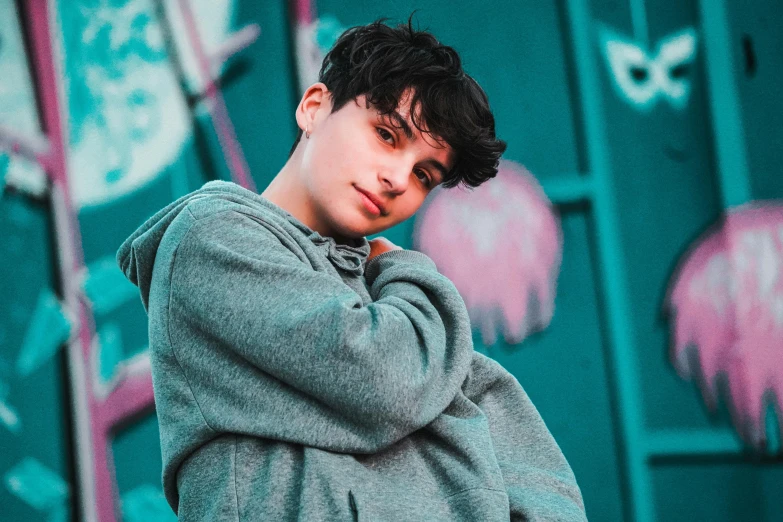 a young man standing in front of a graffiti covered wall, an album cover, inspired by John Luke, trending on pexels, beautiful androgynous girl, jungkook, machenic, baggy eyes