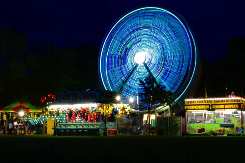 a carnival at night with a ferris wheel in the background, by The Family Circus, blue and green light, multi - coloured