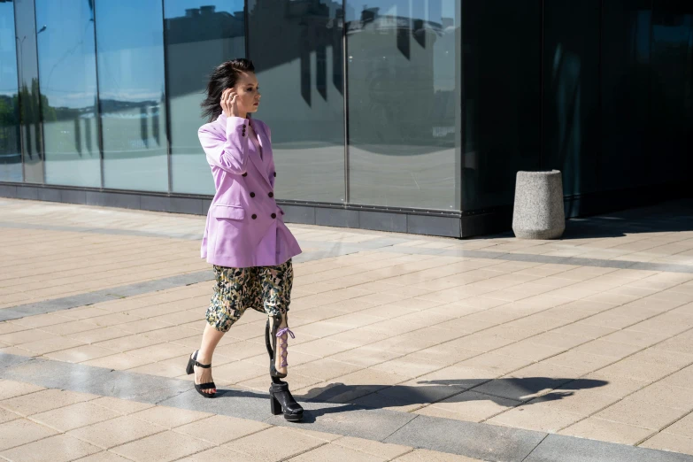 a woman walking down a sidewalk talking on a cell phone, trending on pexels, baroque, a purple suit jacket, björk, taken with sony alpha 9, at the waterside