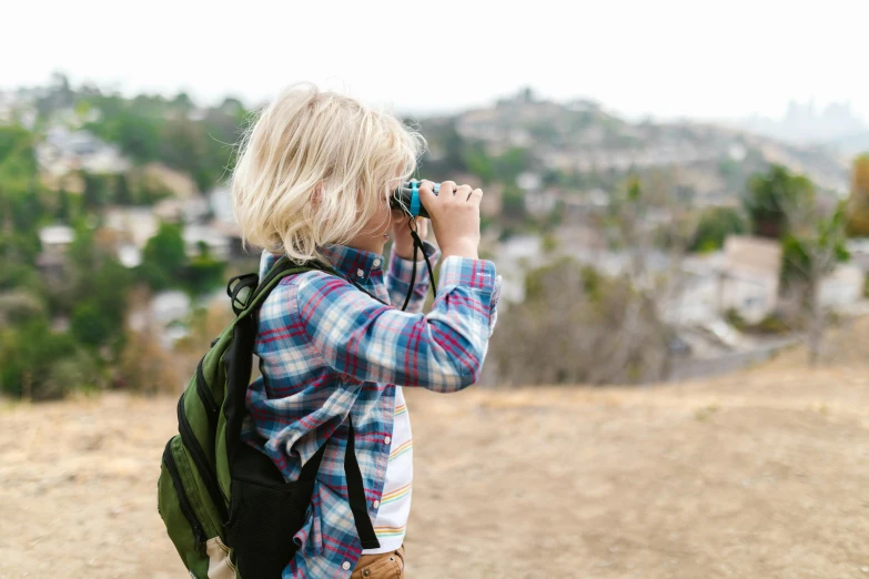 a little girl taking a picture with a camera, a picture, by Winona Nelson, pexels, visual art, hiking clothes, looking over city, is looking at a bird, hills