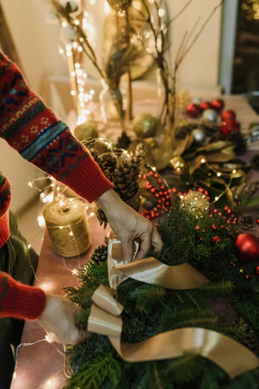 a woman decorating a christmas wreath on a table, pexels contest winner, cozy lighting, full - color, dramatic details, entertaining