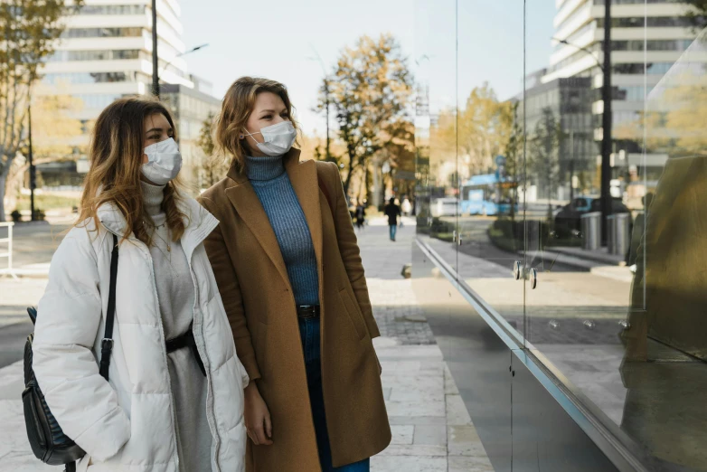 a couple of women standing next to each other on a sidewalk, trending on pexels, masked doctors, air pollution, hunting, looking outside