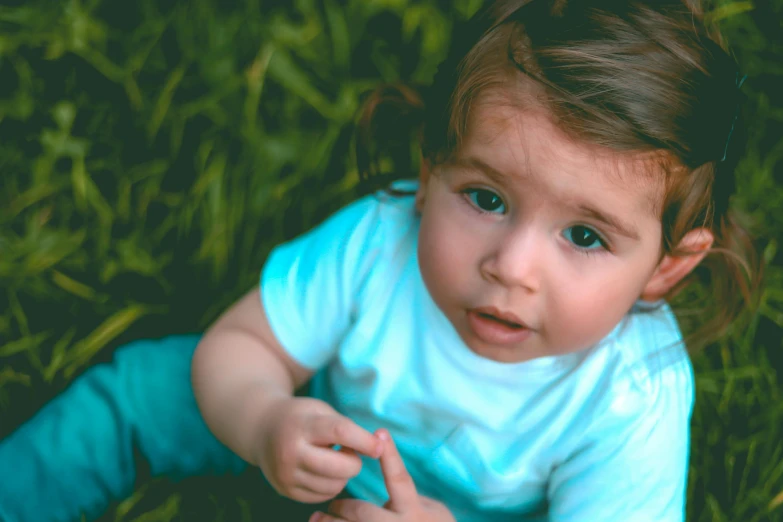 a little girl that is sitting in the grass, pexels contest winner, serious expressions, teal color graded, cute young man, thumbnail