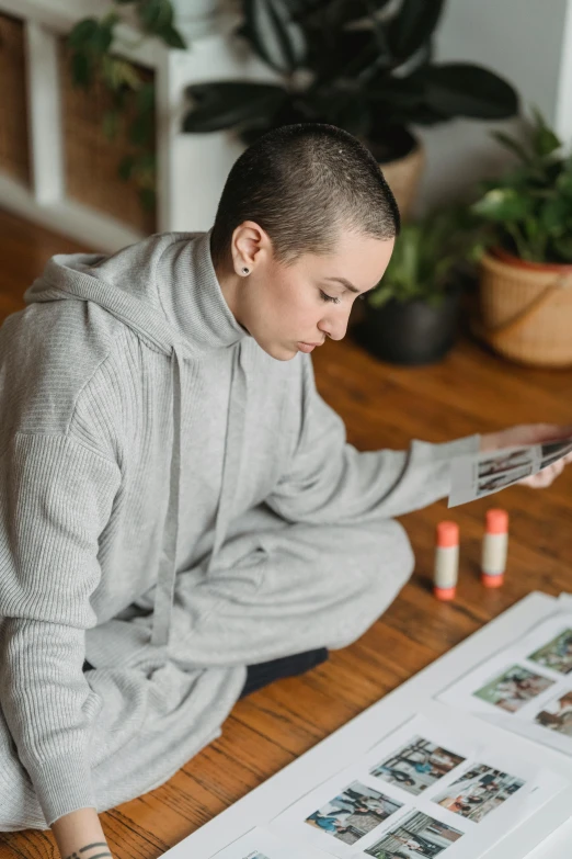 a woman sitting on the floor reading a magazine, a picture, by Julia Pishtar, pexels contest winner, visual art, buzz cut, gray hoodie, wearing a track suit, on a desk