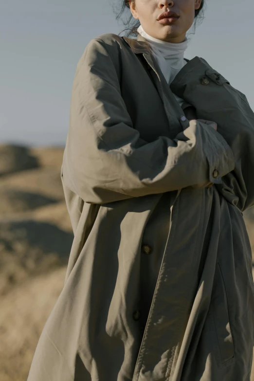 a woman standing in the desert with her arms crossed, unsplash, visual art, he is wearing a trenchcoat, muted green, gray men, detail shot