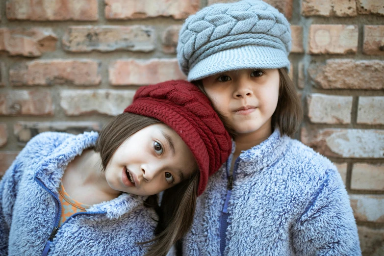 a couple of young girls standing next to each other, by Lilia Alvarado, unsplash, wearing wool hat, wine-red and grey trim, two long braids blue, mini model