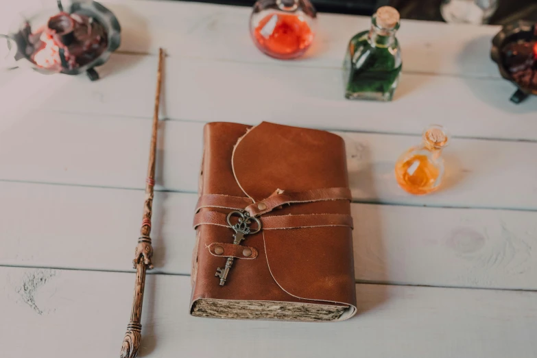 a book sitting on top of a table next to a wand, inspired by Hermione Hammond, unsplash, renaissance, leather pouch, full front view, delightful surroundings, rustic