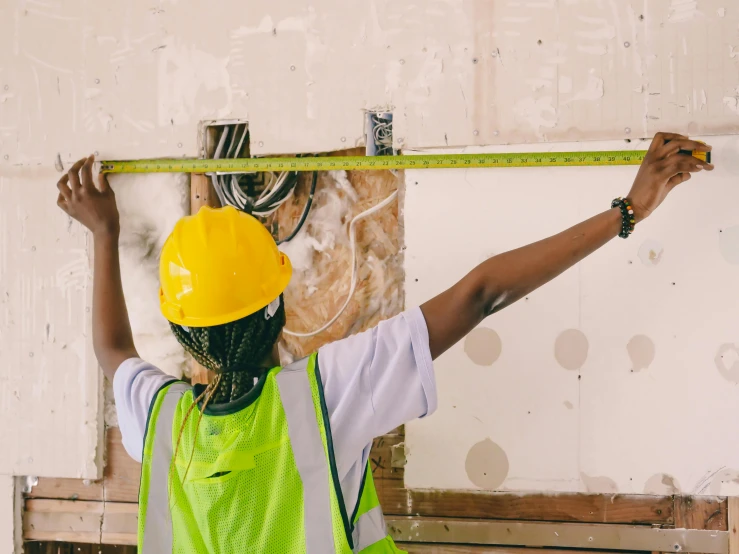 a construction worker measuring a wall with a tape, by Julia Pishtar, pexels contest winner, photo of a black woman, 15081959 21121991 01012000 4k, wearing hi vis clothing, on a yellow canva