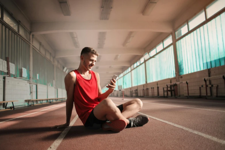 a man sitting on the ground looking at his cell phone, pexels contest winner, red sport clothing, indoor picture, avatar image, young man with short