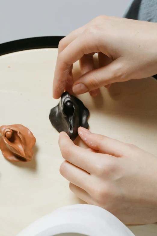 a close up of a person holding a dog toy, a surrealist sculpture, inspired by Kyffin Williams, process art, black and terracotta, made of clay, high angle, female forms