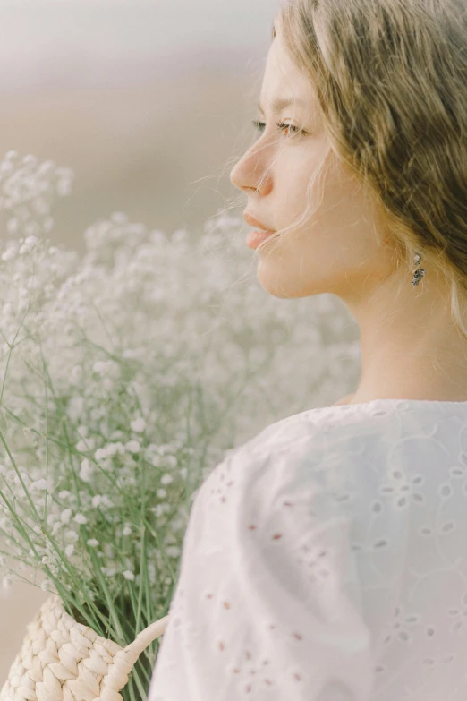 a woman holding a bunch of white flowers, trending on unsplash, aestheticism, gazing off into the horizon, side profile portrait, wearing white clothes, gypsophila