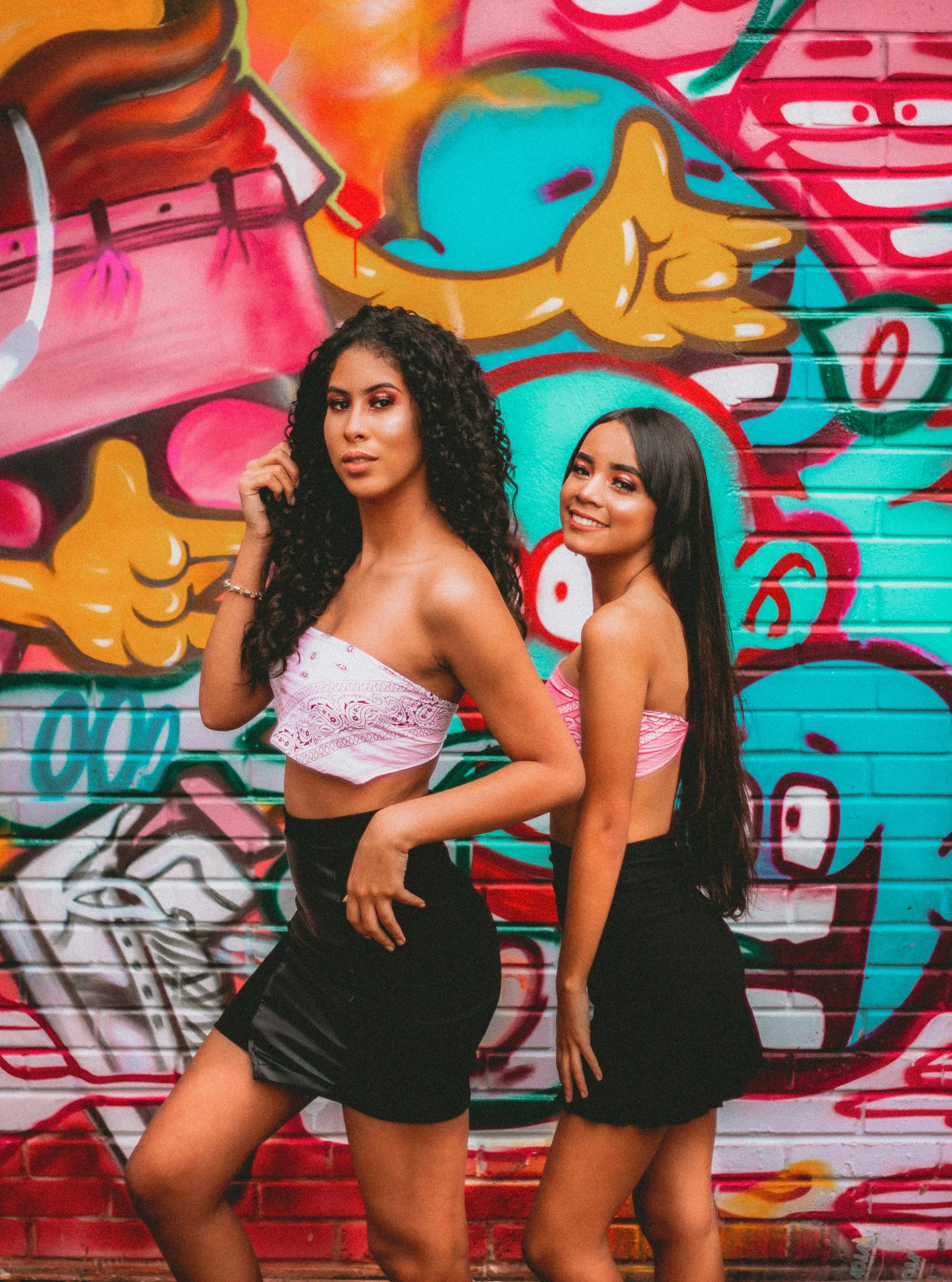 two women standing in front of a graffiti wall, an album cover, trending on pexels, wearing crop top and miniskirt, latina skin, headshot profile picture, photoshoot for skincare brand