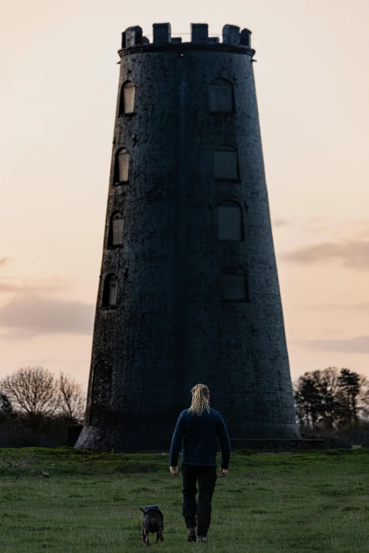 a woman walking her dog in front of a tower, inspired by roger deakins, unsplash, happening, pembrokeshire, 8 k movie still, mausoleum tall ruins, saoirse ronan