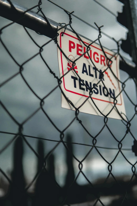 a sign attached to a chain link fence, by Alejandro Obregón, pexels, atmosphere and tension, oily substances, square, promo image