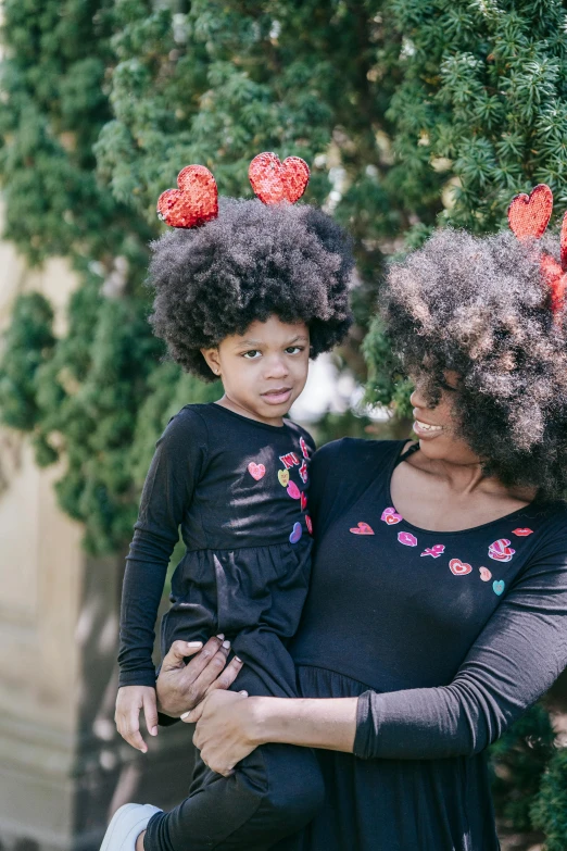 a woman holding a child in her arms, by Winona Nelson, pexels contest winner, long afro hair, red hearts, wig, deep black roots