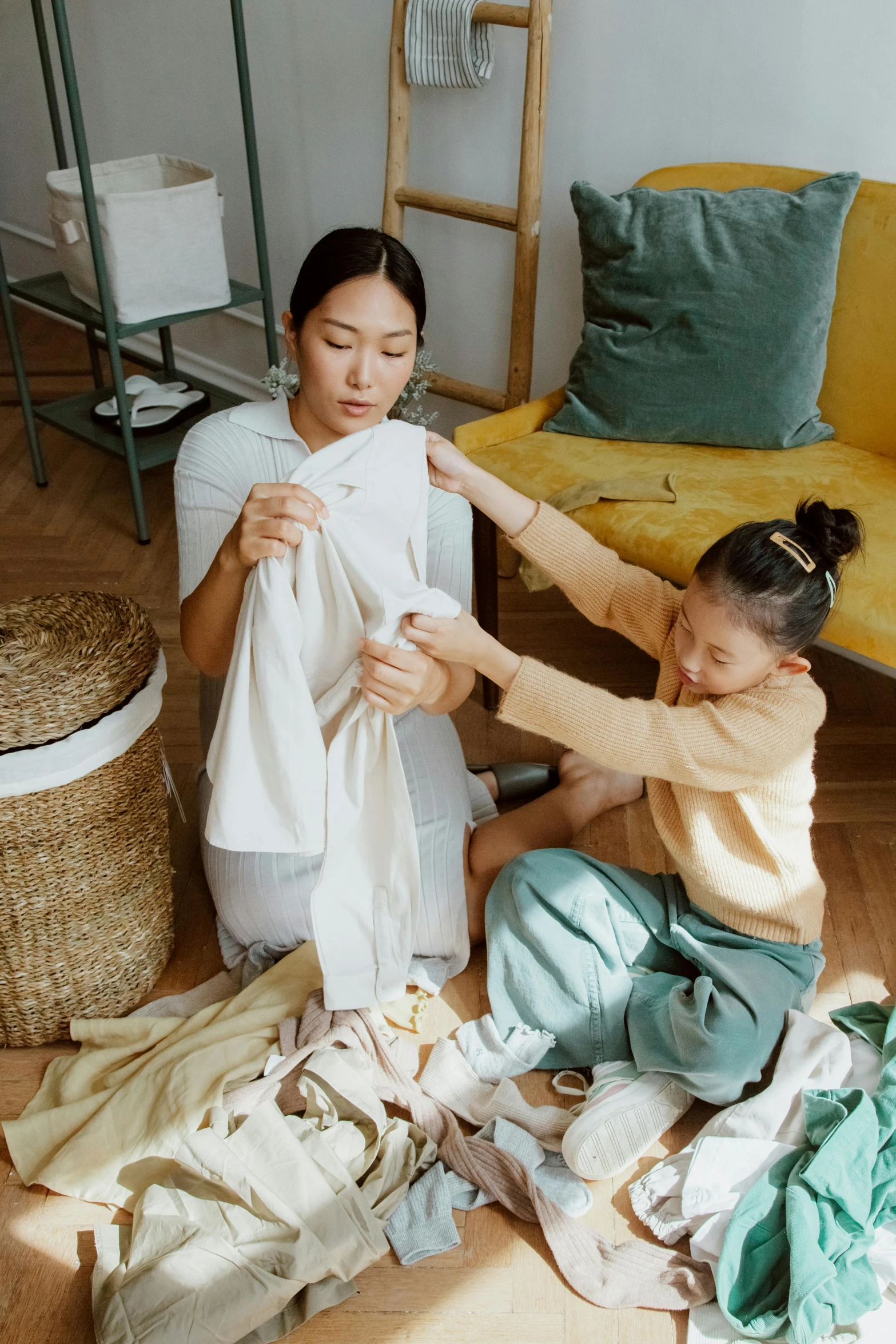 a woman sitting on the floor next to a little girl, touching her clothes, sustainable materials, asian descent, throw