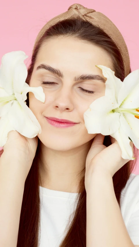 a woman holding two white flowers in front of her face, shutterstock, aestheticism, relaxed eyebrows, beauty campaign, rubrum lillies, eyes closed