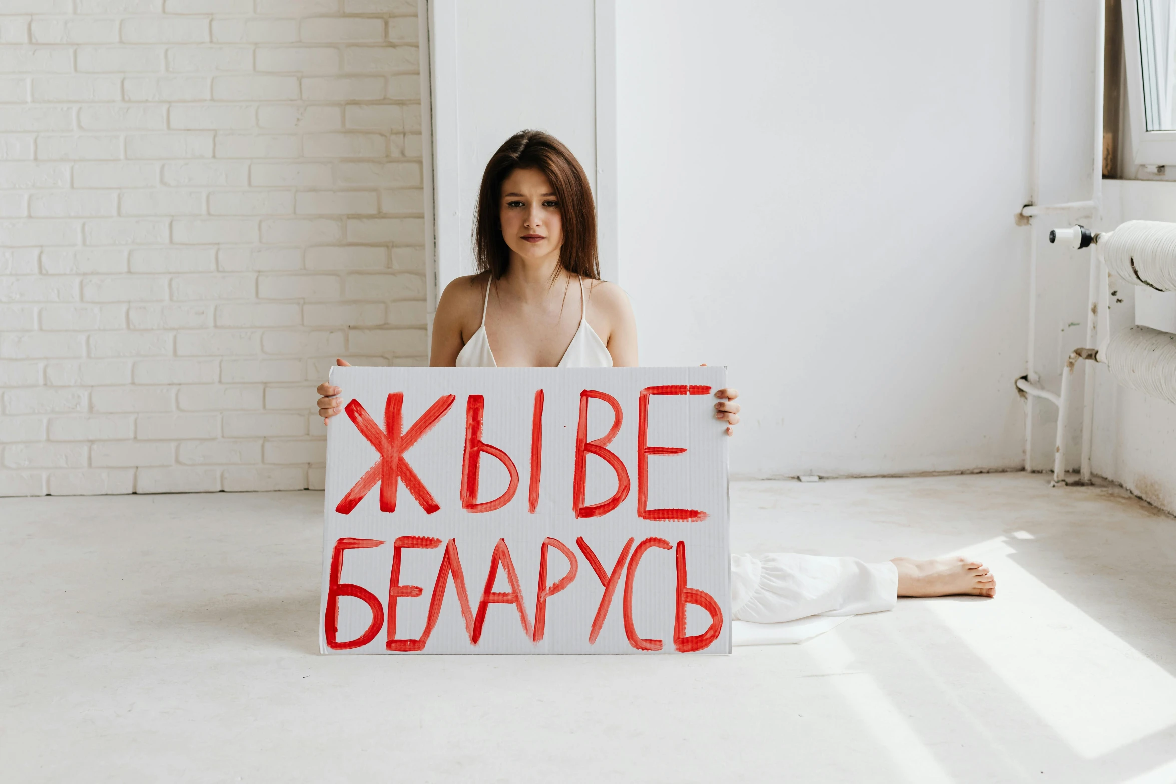 a woman sitting on the floor holding a sign, a poster, by Julia Pishtar, pexels contest winner, feminist art, president of belorussia, young beautiful, background image, 000 — википедия