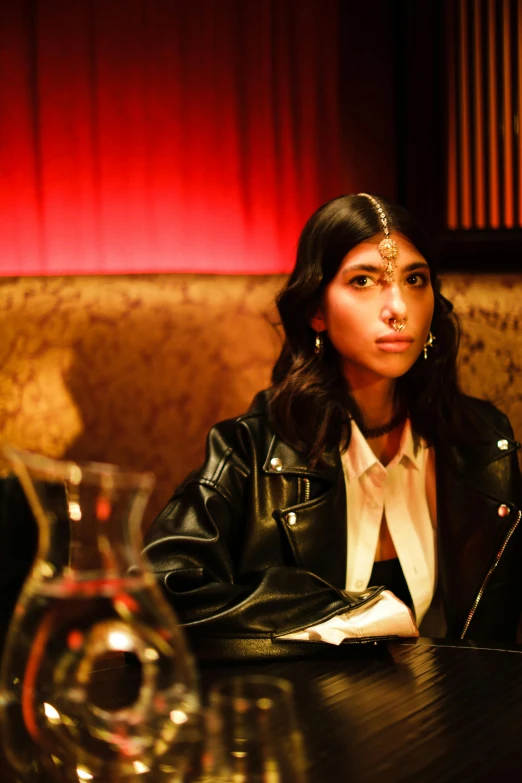 a woman in a leather jacket sitting at a table, an album cover, inspired by Nan Goldin, trending on pexels, mia khalifa, scene from a dinner party, serious look, [ theatrical ]