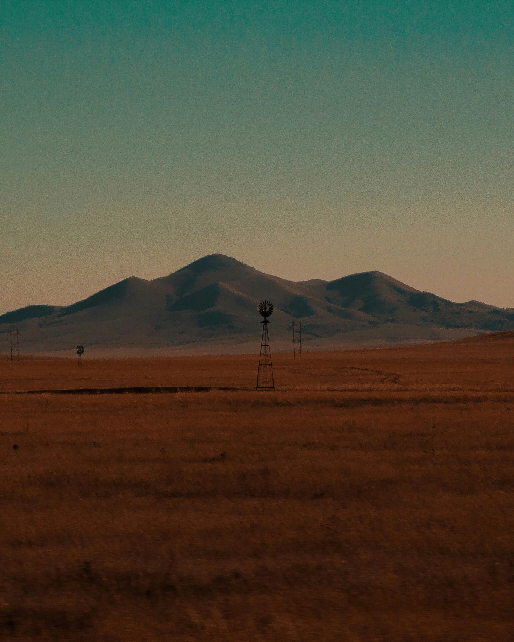 a windmill in a field with mountains in the background, an album cover, inspired by Elsa Bleda, unsplash contest winner, land art, new mexico desert, still frame the retro twin peaks, view from a distance, late evening